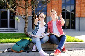 2 students sitting outside school with thumbs up